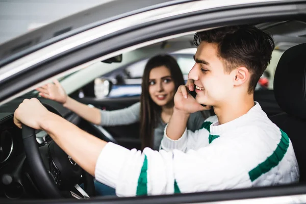 Jovem mostrando uma estrada na frente do carro, enquanto o motorista usando um telefone celular e perder a concentração. Condução perigosa . — Fotografia de Stock
