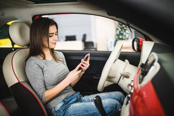 Jovem mulher enviando mensagens enquanto dirige em um carro novo — Fotografia de Stock