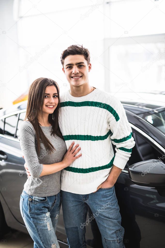 Beautiful young couple standing at the car dealership and making their decision