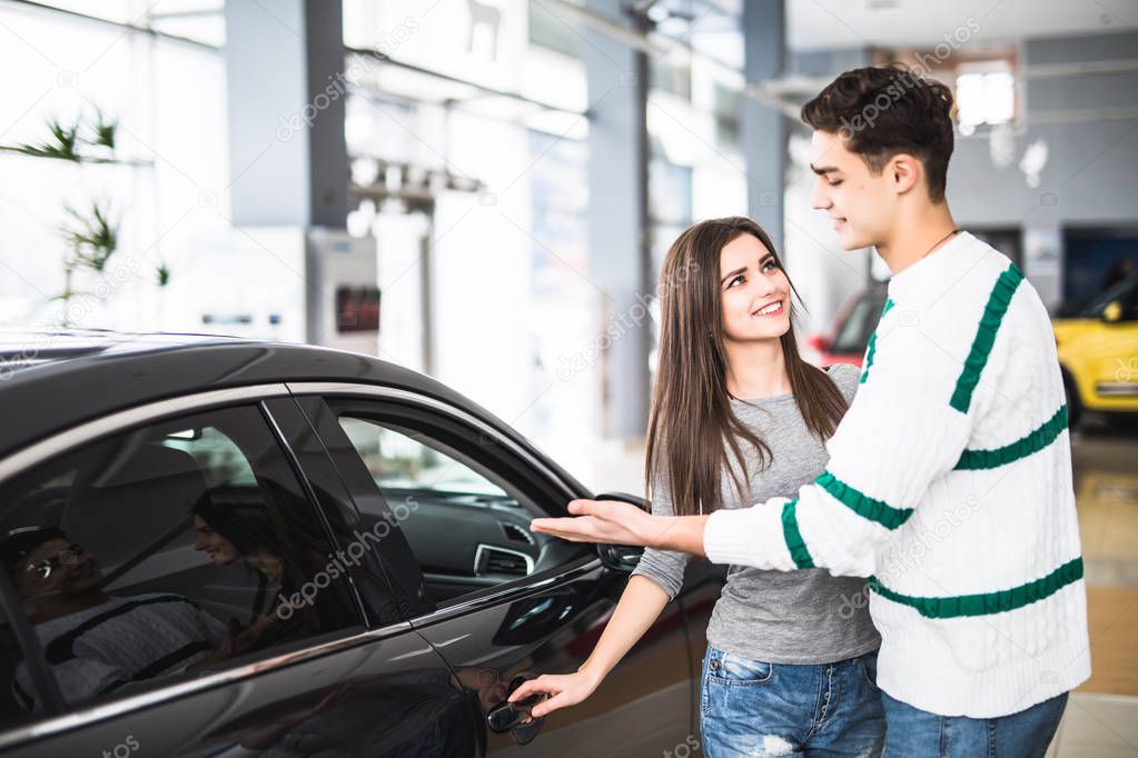 Beautiful young couple standing at the dealership choosing the car to buy