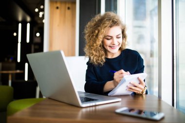 Mutlu curlu genç kadın parlak windows ile modern yerde dizüstü bilgisayar kullanmak.