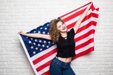 Güzel genç kıvırcık kız poz ve gülümseyen rahat kıyafetler, ayakta duvara karşı Amerikan bayrağı ile kaplı