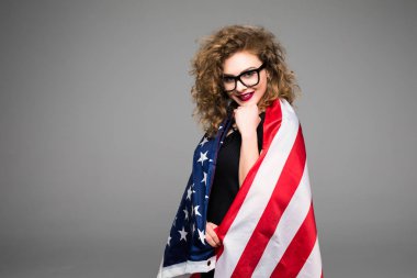 Amerikan bayrağı kapalı ve gri arka plan üzerinde gülümseyen neşeli genç kadın rahat kıyafetler ve gözlük