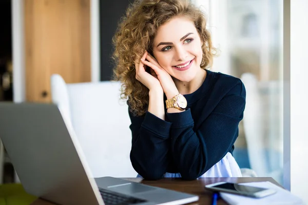 Mujer atractiva joven en un escritorio de oficina moderno, trabajando con el ordenador portátil, mirando a la ventana, pensando en un post . — Foto de Stock