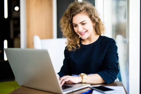 Feliz rizo joven uso de la computadora portátil en el lugar moderno con ventanas brillantes . — Foto de Stock