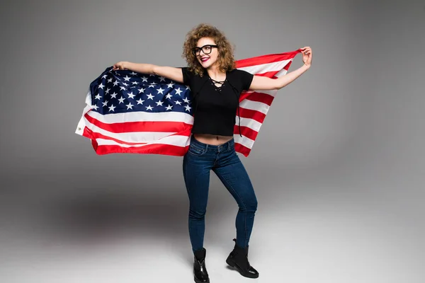Glad ung kvinna i casual kläder är våg den amerikanska flaggan och leende på grå bakgrund — Stockfoto