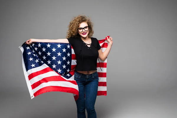 Веселая молодая женщина в повседневной одежде держит американский флаг и улыбается на сером фоне — стоковое фото