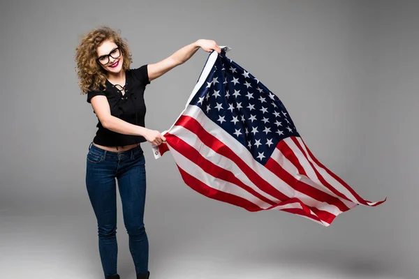 Joven alegre en ropa casual es ondear la bandera americana y sonreír sobre fondo gris — Foto de Stock