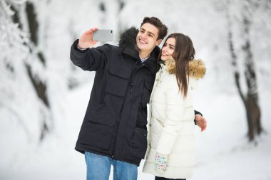 Selfie fotoğraf genç Romantik Çift gülümseme kar orman açık kış çam ormanlarının alarak adam. Selfie çiftiz.