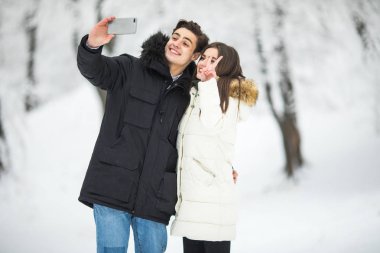 Selfie fotoğraf genç Romantik Çift gülümseme kar orman açık kış çam ormanlarının alarak adam. Selfie çiftiz.