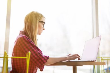 Dizüstü bilgisayar kullanan ve tipik klavye tarafından ofisinde oturan yan portre genç kadın işçi