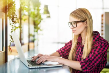 Genç kadın girişimci çalışma oturma bir ofiste onun dizüstü bilgisayarda yazarak bir masada taraftan göster