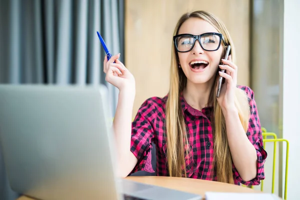 Mujer bastante joven sentada en su lugar de trabajo, usando su computadora portátil con expresión facial feliz . — Foto de Stock