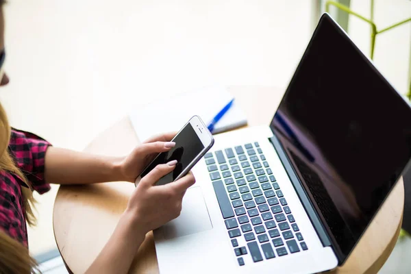 Close-up van vrouwelijke handen met behulp van slimme telefoon terwijl u werkt op computer op moderne kantoor interieur — Stockfoto