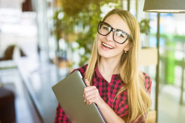 Hermosa mujer independiente en ropa casual inteligente con un ordenador portátil, mirando a la cámara y sonriendo en la oficina moderna — Foto de Stock