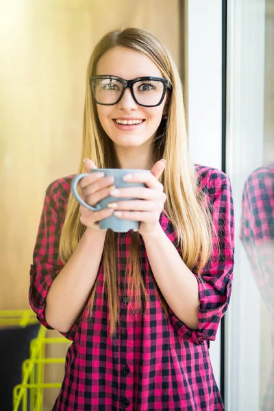 Young girl with cup of coffee with good mood in the morning in modern office near window — Stock Photo, Image