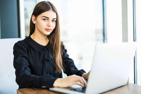 Vacker ung kvinna som arbetar på den bärbara datorn och tittar på kameran i café — Stockfoto