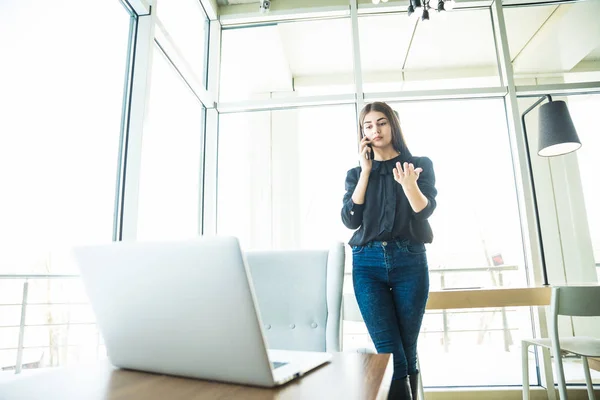 노트북 테이블 근처 전화에서 얘기 하는 캐주얼 옷에 비즈니스 우먼 — 스톡 사진