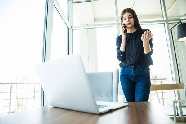 Mujer de negocios hablando por teléfono cerca de la mesa y mirando el portátil — Foto de Stock