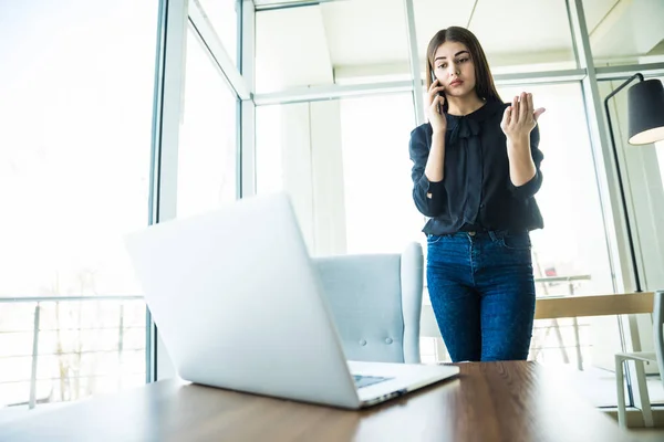 Mujer de negocios hablando por teléfono cerca de la mesa y mirando el portátil — Foto de Stock