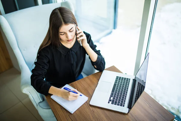 Joven mujer de negocios sentada en la mesa. Mujer firmar documentos, mantener el gráfico y el uso de teléfono inteligente en la mesa es ordenador portátil y tableta . — Foto de Stock