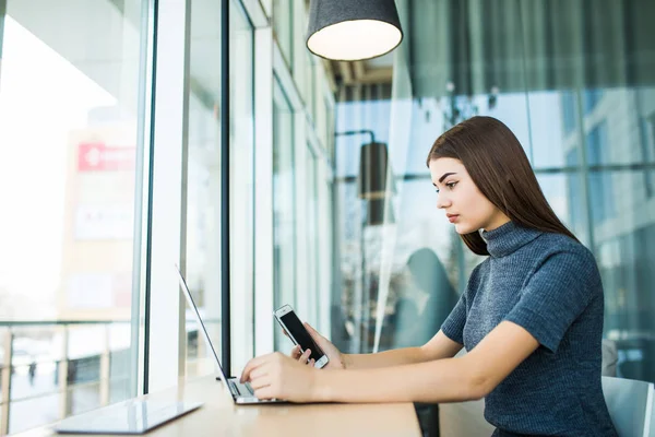 Sidovy av brunett kvinna använder bärbar dator sitter mot stora fönster i office — Stockfoto