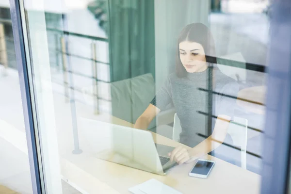 Mujer joven hablando por teléfono y utilizando la tableta a través de la ventana — Foto de Stock