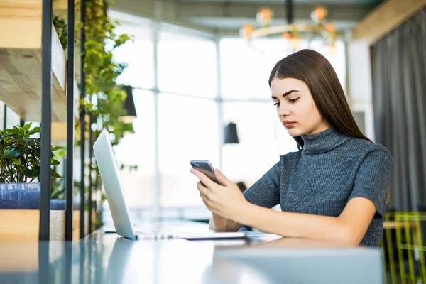 Ung vacker kvinna som bär glasögon, arbeta på kontoret, använder en bärbar dator och mobiltelefon — Stockfoto