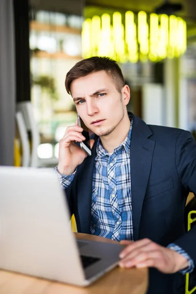 Joven freelancer trabajando con laptop y hablando por teléfono con el cliente — Foto de Stock