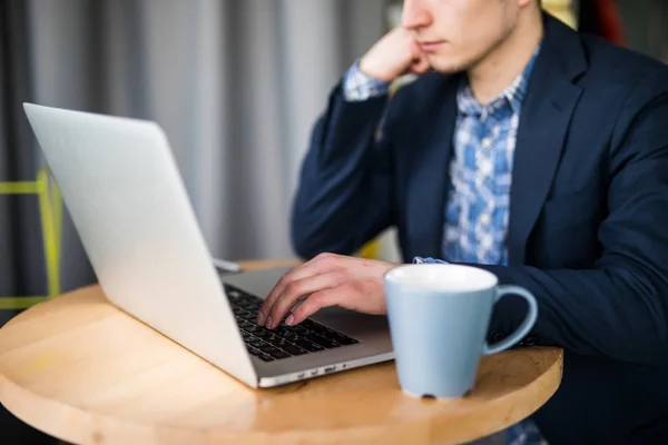 Homme d'affaires ou pigiste travaillant sur ordinateur portable sur bureau blanc avec téléphone intelligent et livres au bureau à domicile, gros plan . — Photo