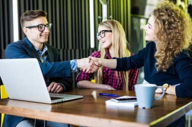 Genç öğrenciler araçları kullanma, söz ve modern ofiste çalışırken gülümseyerek. Erkek ve kadın el sıkışma vardır