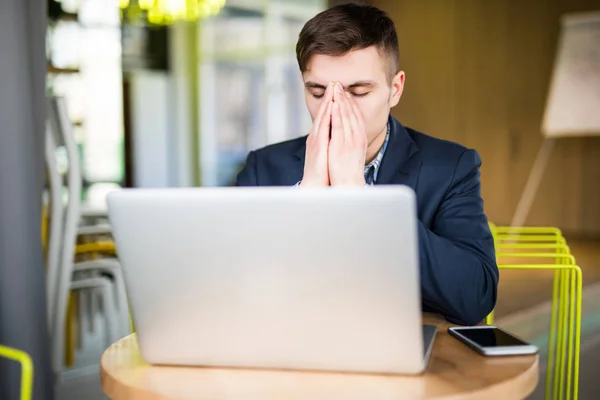 Frustrierter junger Mann massiert seine Nase und hält die Augen geschlossen, während er an seinem Arbeitsplatz im Büro sitzt — Stockfoto