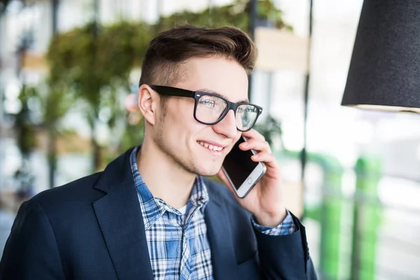 Retrato de hombre caucásico atractivo en camisa casual y gafas hablando por teléfono celular en el lugar de trabajo . — Foto de Stock