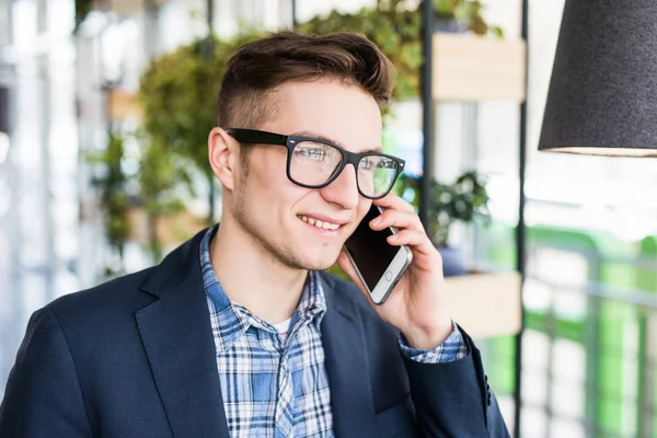 Retrato de hombre caucásico atractivo en camisa casual y gafas hablando por teléfono celular en el lugar de trabajo . — Foto de Stock