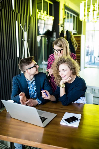 Drie jonge mensen werken samen aan een nieuw project. Team van gelukkig office mensen werken op laptopcomputer, glimlachend. — Stockfoto