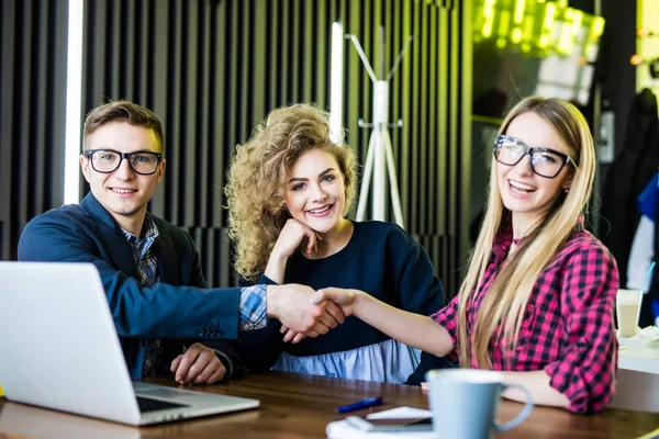 Jonge studenten zijn met behulp van gadgets, praten en glimlachen terwijl hij werkte bij het moderne kantoor. Mannen en vrouw zijn handshaking — Stockfoto