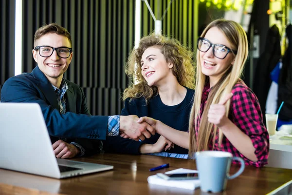 Jonge studenten zijn met behulp van gadgets, praten en glimlachen terwijl hij werkte bij het moderne kantoor. Mannen en vrouw zijn handshaking — Stockfoto