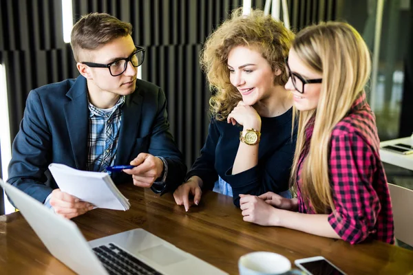 Groep vrienden bezig met hun kleine moderne kantoor. Man show op zijn aankondiging op laptop — Stockfoto