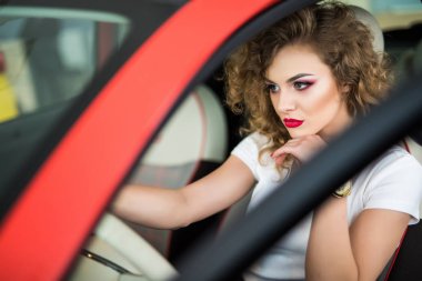 Kırmızı arabada oturan gülümseyen kadın