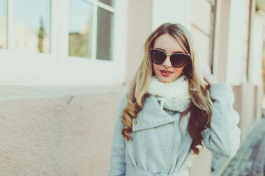 Mutlu ve neşeli, sarışın genç güneş gözlüğü modeli veya öğrenci hafif ceket dışında doğal sokak arka plan üzerinde gülümseyen.