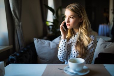 Cep telefonu üzerinde konuşurken ve kafede masada kahve içme genç kadın