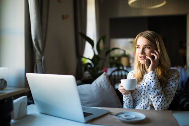 Bir kafede onu telefon ve dizüstü kullanarak sarışın genç iş kadını