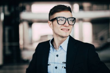 Genç işadamı giyen gözlük, uzak ofis binası karşı arıyorsunuz gülümseyerek kapatın