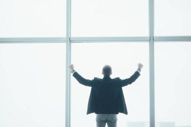 Şık iş adamı rised eller zafer büyük bir pencere arka planda