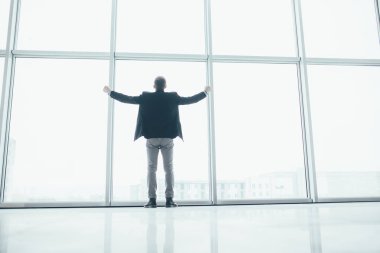 Şık iş adamı rised eller zafer büyük bir pencere arka planda