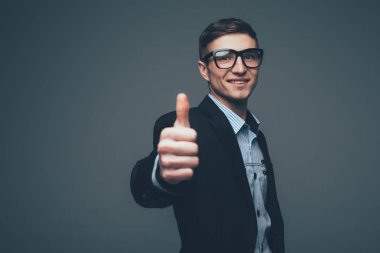 Koyu takım elbise ceket gri arka plan üzerinde iki başparmak yukarıya ile sırıtan adam. Kopya alanı içerir.