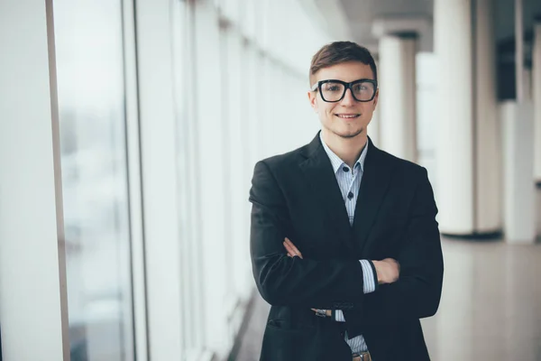 Hombre de negocios seguro de pie con las manos cruzadas contra las ventanas de la oficina — Foto de Stock