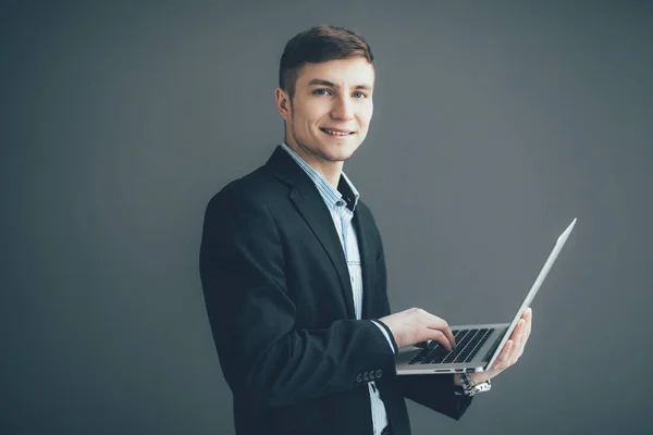 Pohledný mladý podnikatel používá notebook, při pohledu na fotoaparát a usmívá se na černém pozadí — Stock fotografie