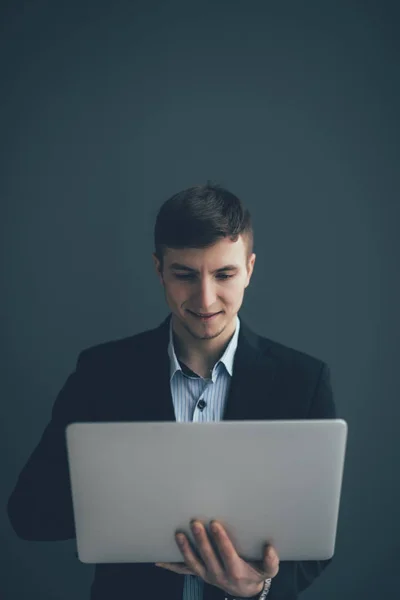 Guapo joven empresario está utilizando un ordenador portátil, mirando a la cámara y sonriendo, sobre fondo negro — Foto de Stock