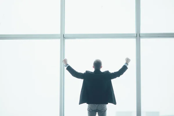 Eleganta affärsman i hörigt händer seger i bakgrunden av ett stort fönster — Stockfoto